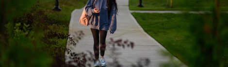 Student walking into campus from parking lot on a sunny day.