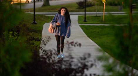 Student walking into campus from parking lot on a sunny day.