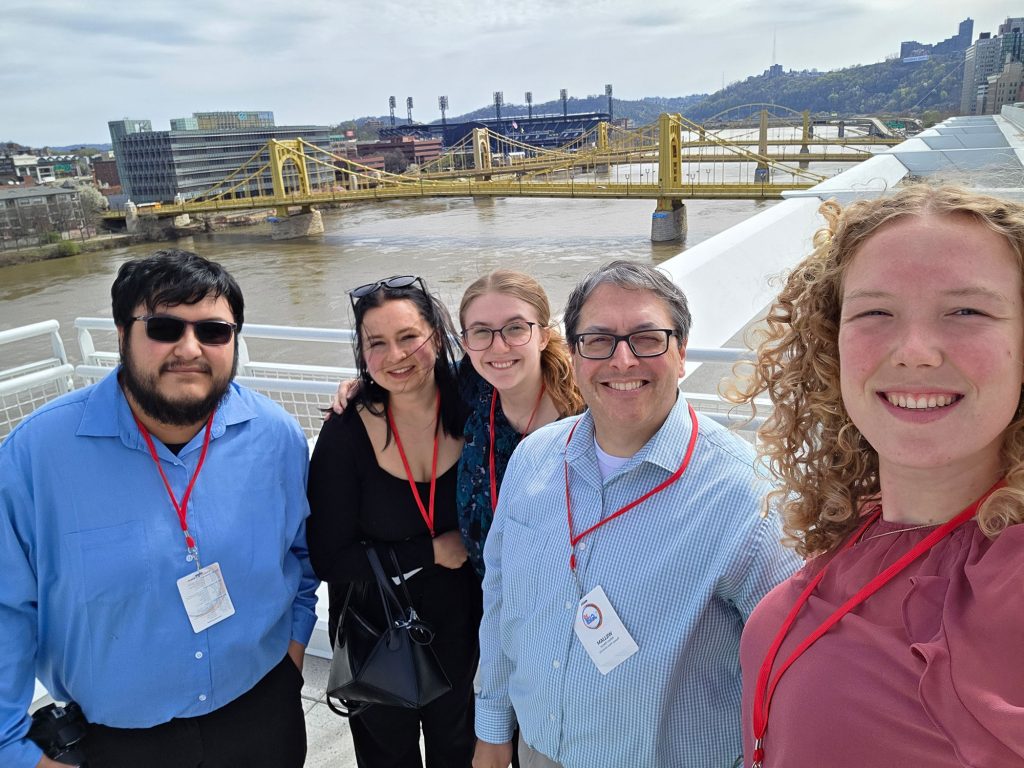 Thomas More student researchers Madison Genslinger, Eva Kinwel, Paige Robbins, and Jose Ruiz with Professor William Wetzel, Ph.D. take a selfie along the river in Pittsburgh.
